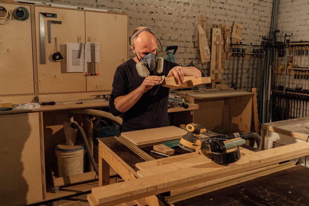 Experienced carpenter wearing a mask while working with wood in a well-equipped workshop.